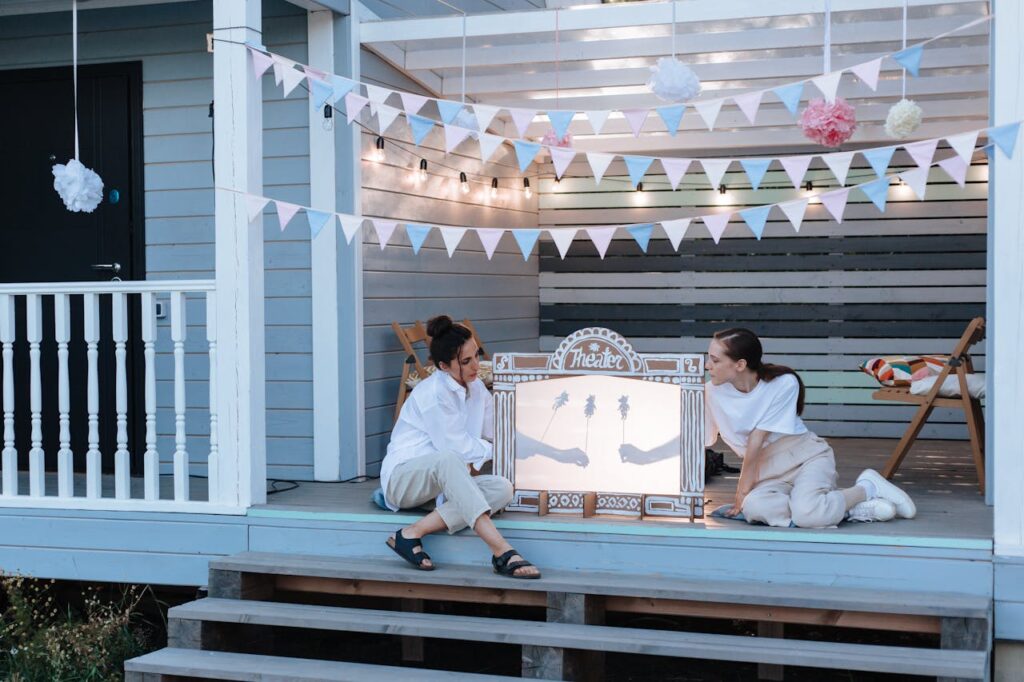 pexels photo 10045498 Two women enjoy an outdoor shadow puppet show on a porch decked with decorative pennants.