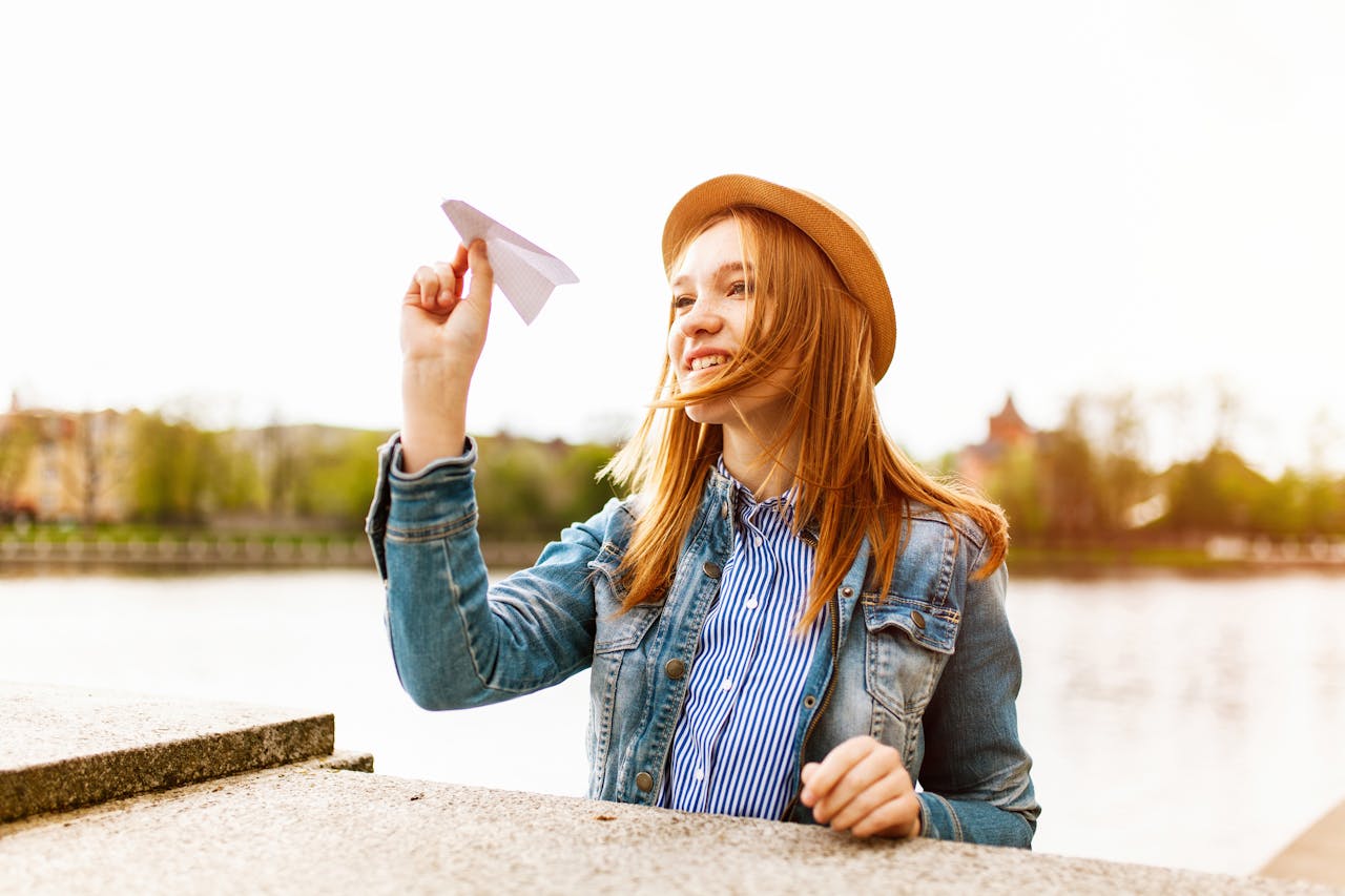 Woman enjoying a sunny day by the water holding a paper plane.