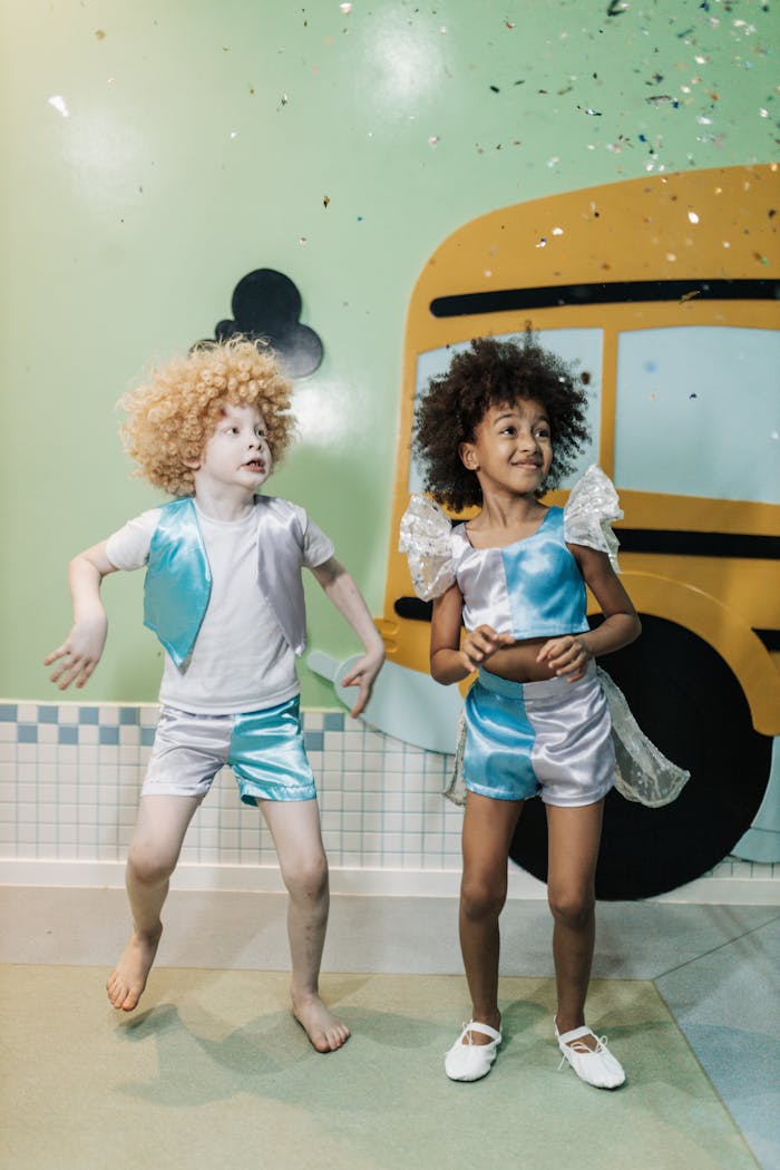 Two children in playful costumes posing joyfully indoors near a school bus backdrop.