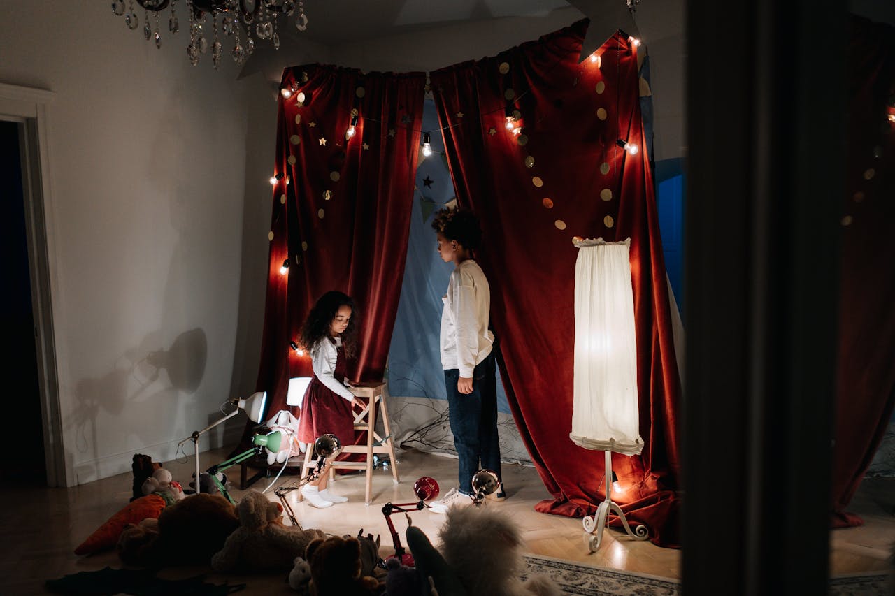 Two children performing a play in a creatively decorated home theater with red curtains.