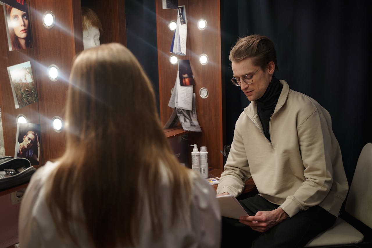 Actors reviewing scripts backstage in a theatrical dressing room setting.