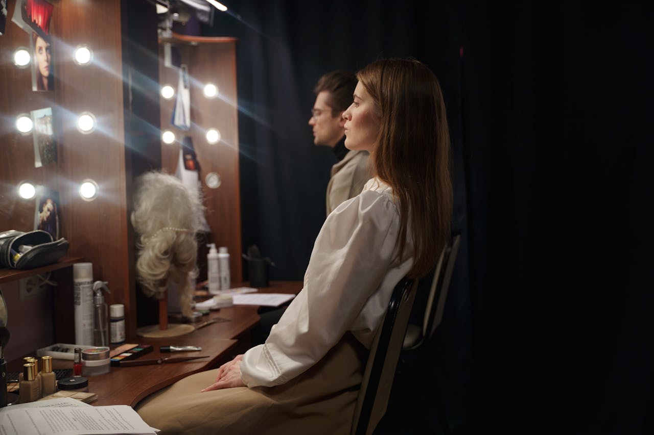 Two actors in a theater dressing room preparing for a performance, sitting and reviewing scripts.
