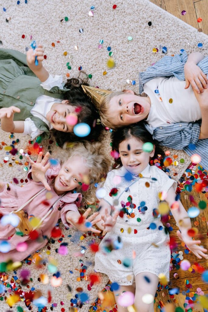 pexels photo 8104208 Four happy children enjoy a party, lying on the floor with colorful confetti showering around them.